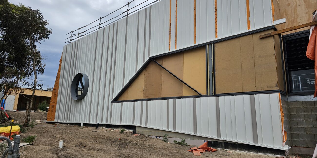 view of a round window on a school building, framed by detailed and expertly installed metal cladding, showcasing intricate craftsmanship and a sleek, modern design.