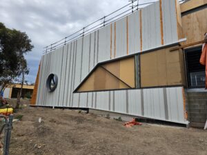 view of a round window on a school building, framed by detailed and expertly installed metal cladding, showcasing intricate craftsmanship and a sleek, modern design.